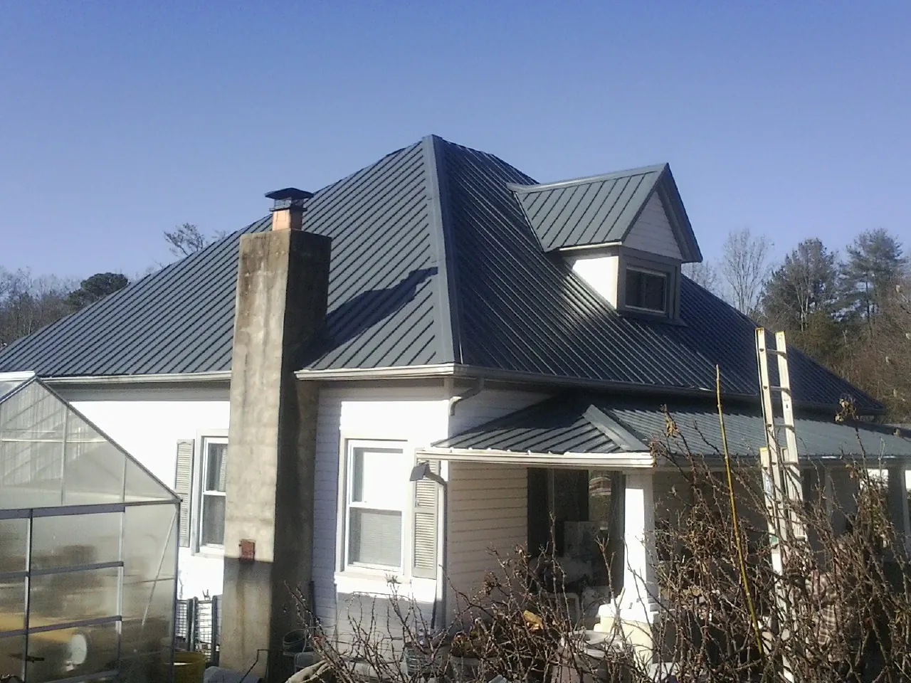 Dark blue standing seam metal roof on a white farmhouse with dormer — Slate & Tile Roof Repair by Roofing Brothers in Ellenwood