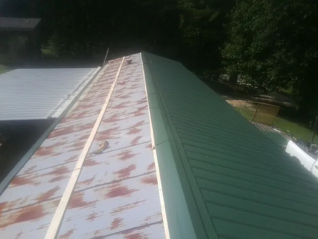 Old rusted panels beside newly installed green metal roofing — Wind Damage Roof Repair by Roofing Brothers in Ellenwood
