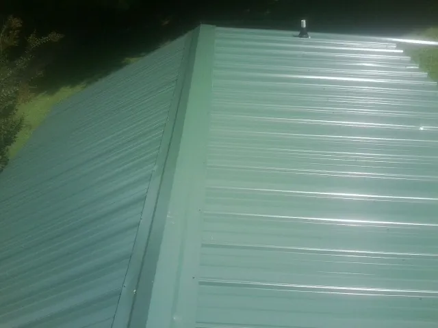New green metal panels meeting at the ridge of a roof — Flat Roof Repair work by our crew in Ellenwood