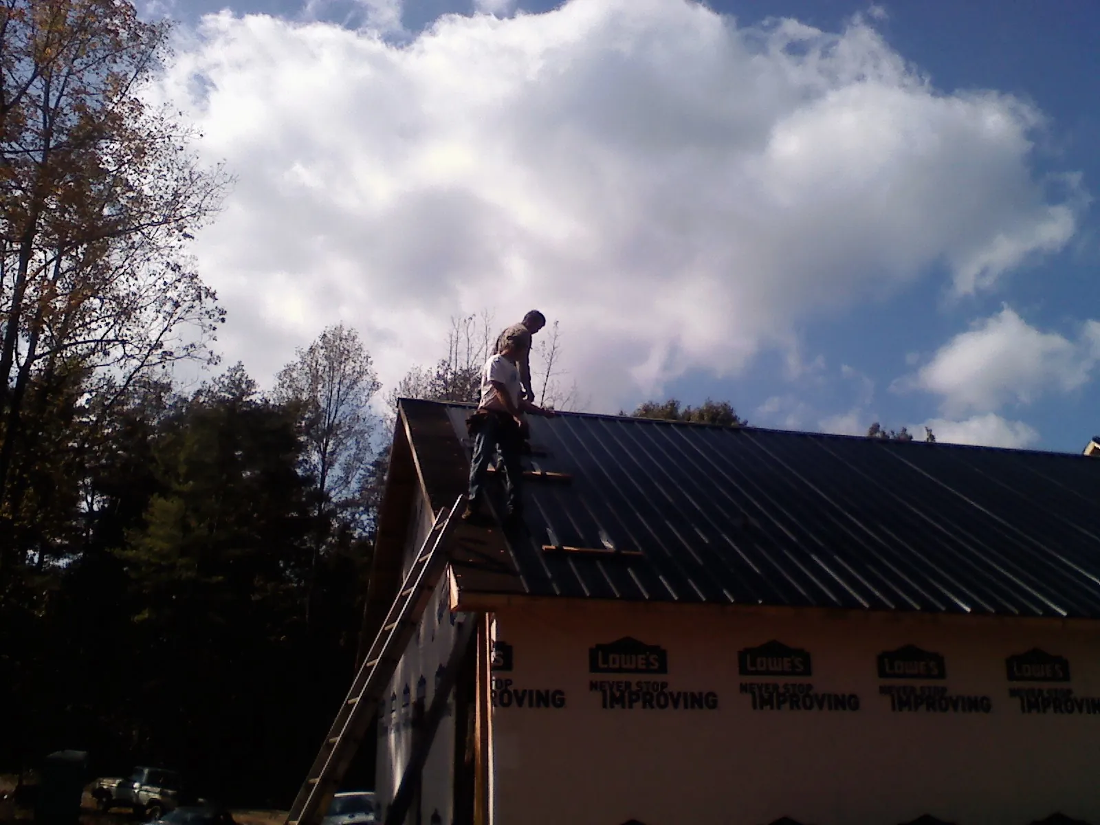 Roofer fastening dark metal panels high against a cloudy sky, from a Roof Inspection job in Ellenwood