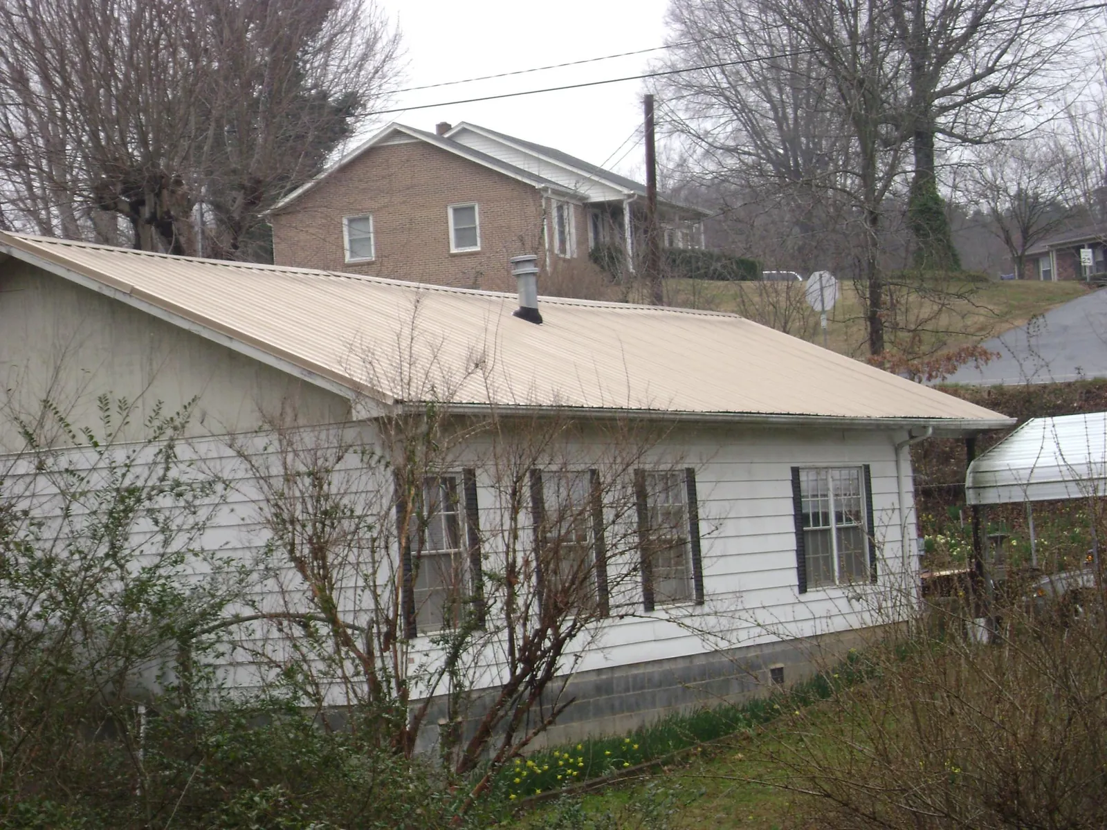 Tan metal roof on a white sided house set into a hillside — Commercial Roofing by Roofing Brothers in Ellenwood