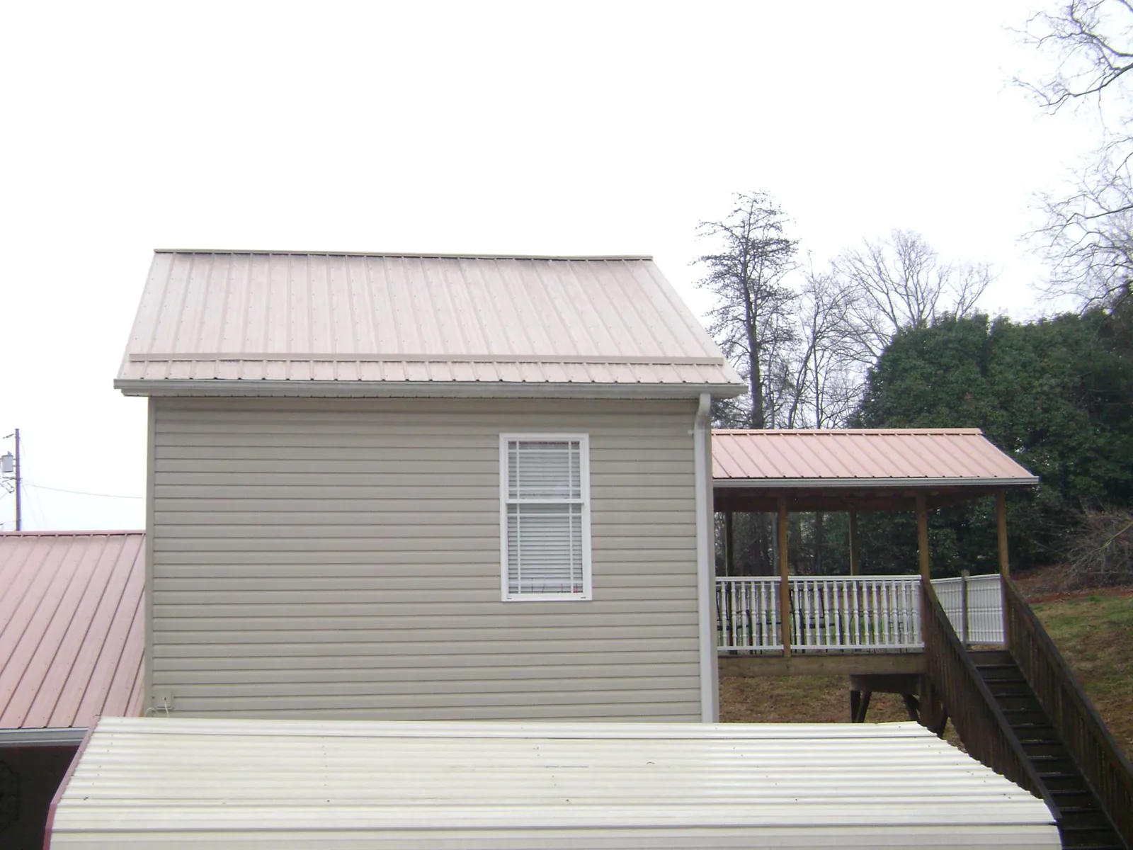 Tan metal roofs on a two story addition and attached porch, from a Roof Replacement job in Ellenwood